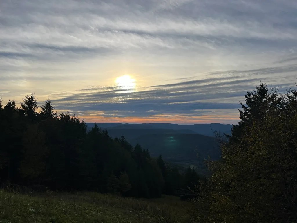 Sunset over a mountainous landscape with trees in the foreground and a colorful sky.