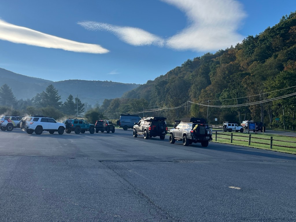 A parking lot filled with various SUVs on a clear morning, surrounded by trees and mountains in the background.