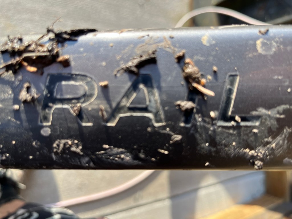Close-up of a dirty black rail with the word 'RAIL' partially obscured by dirt and debris.